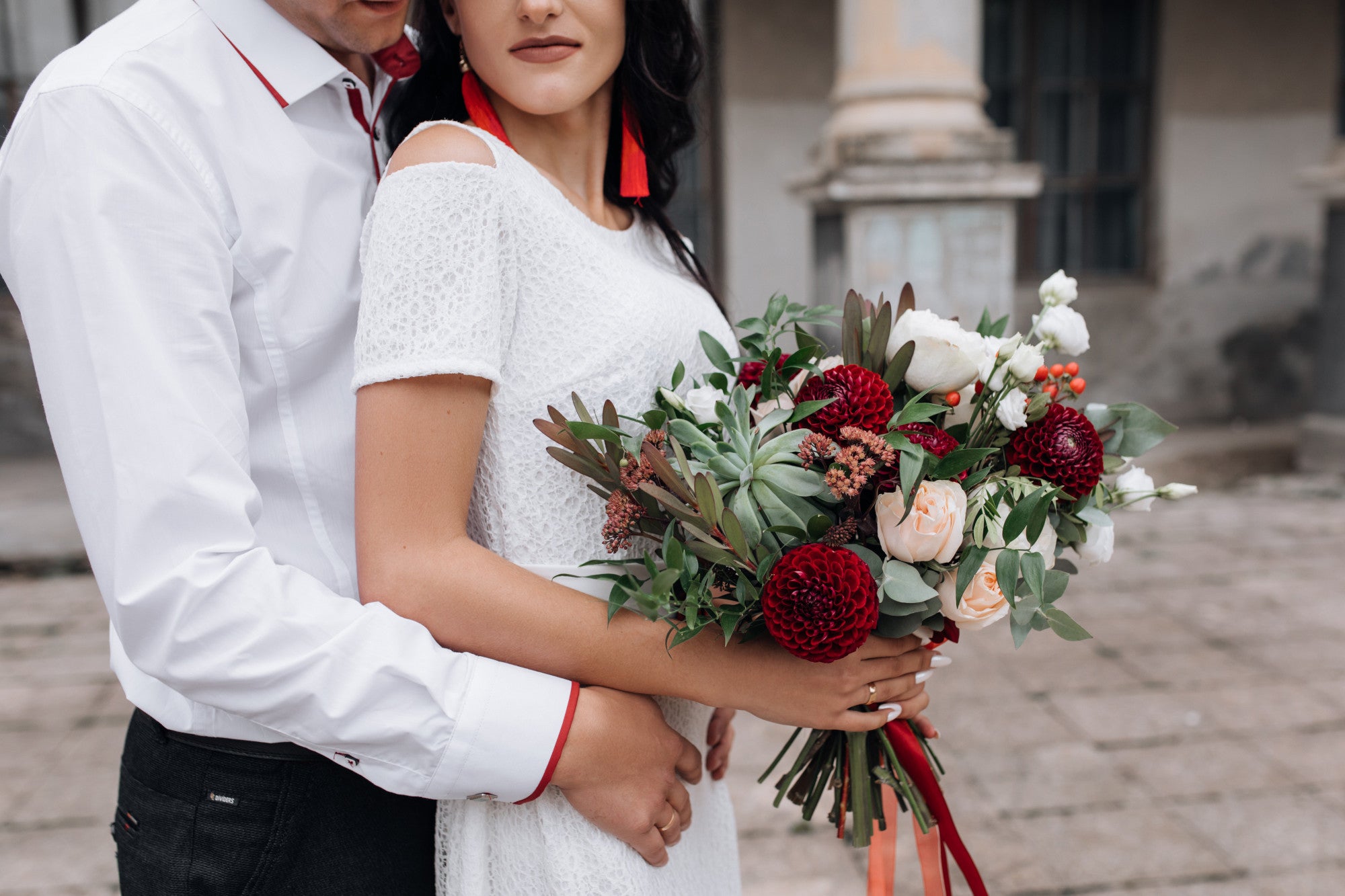 A couple poses with a bouquet of wedding flowers for their big day.