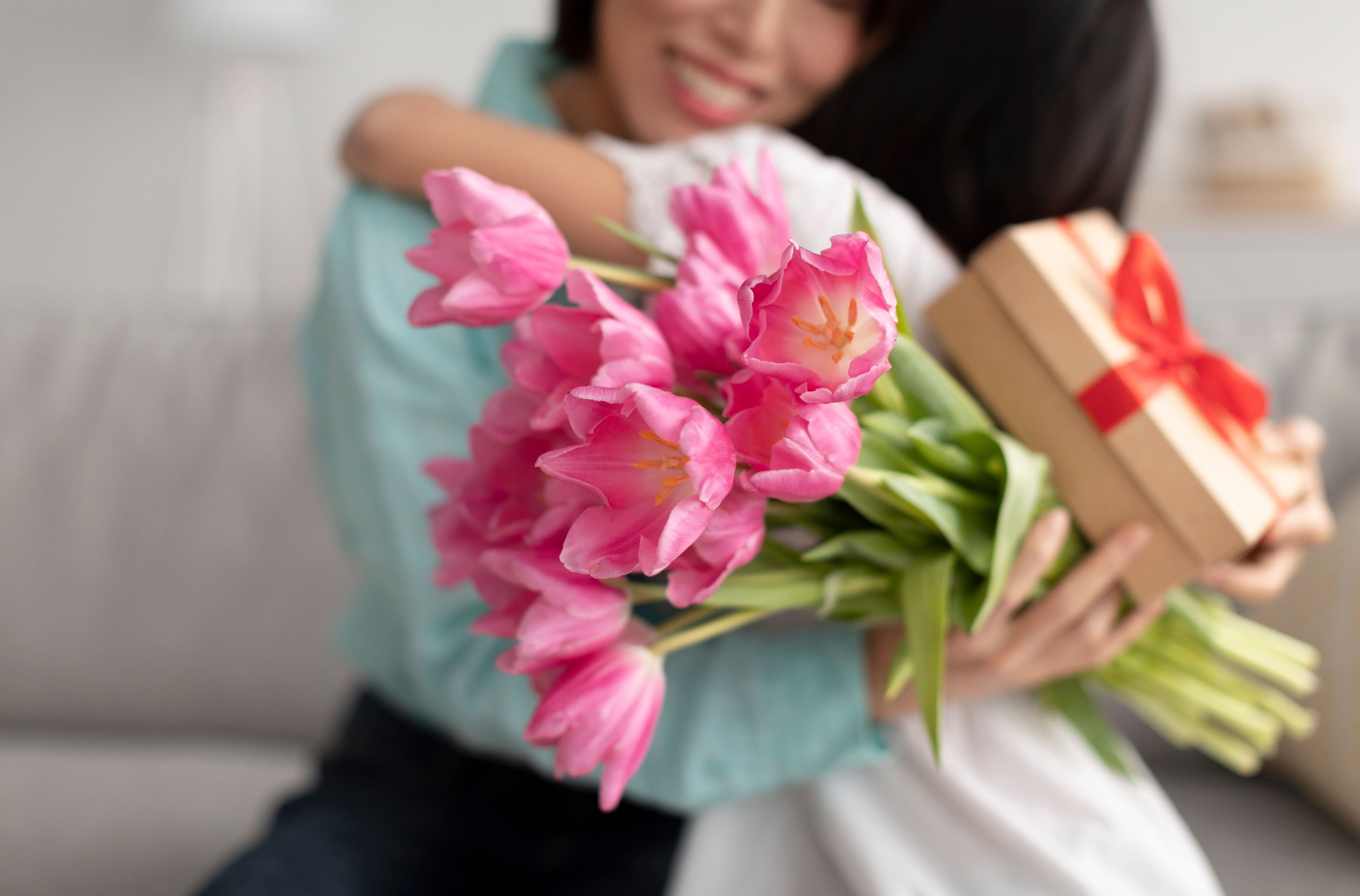 A mother hugs her daughter as she receives flowers and a gift for Mother’s Day.