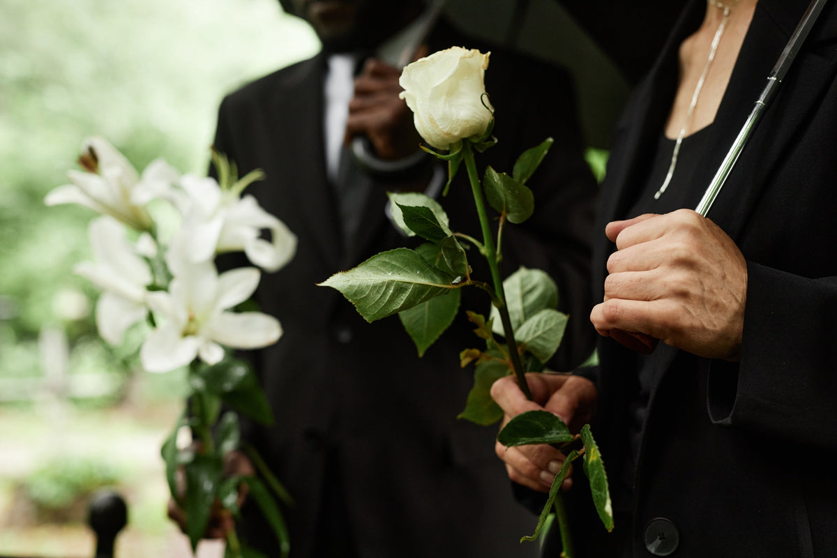 A senior woman and man carrying a white rose and lilies for a sympathy arrangement.