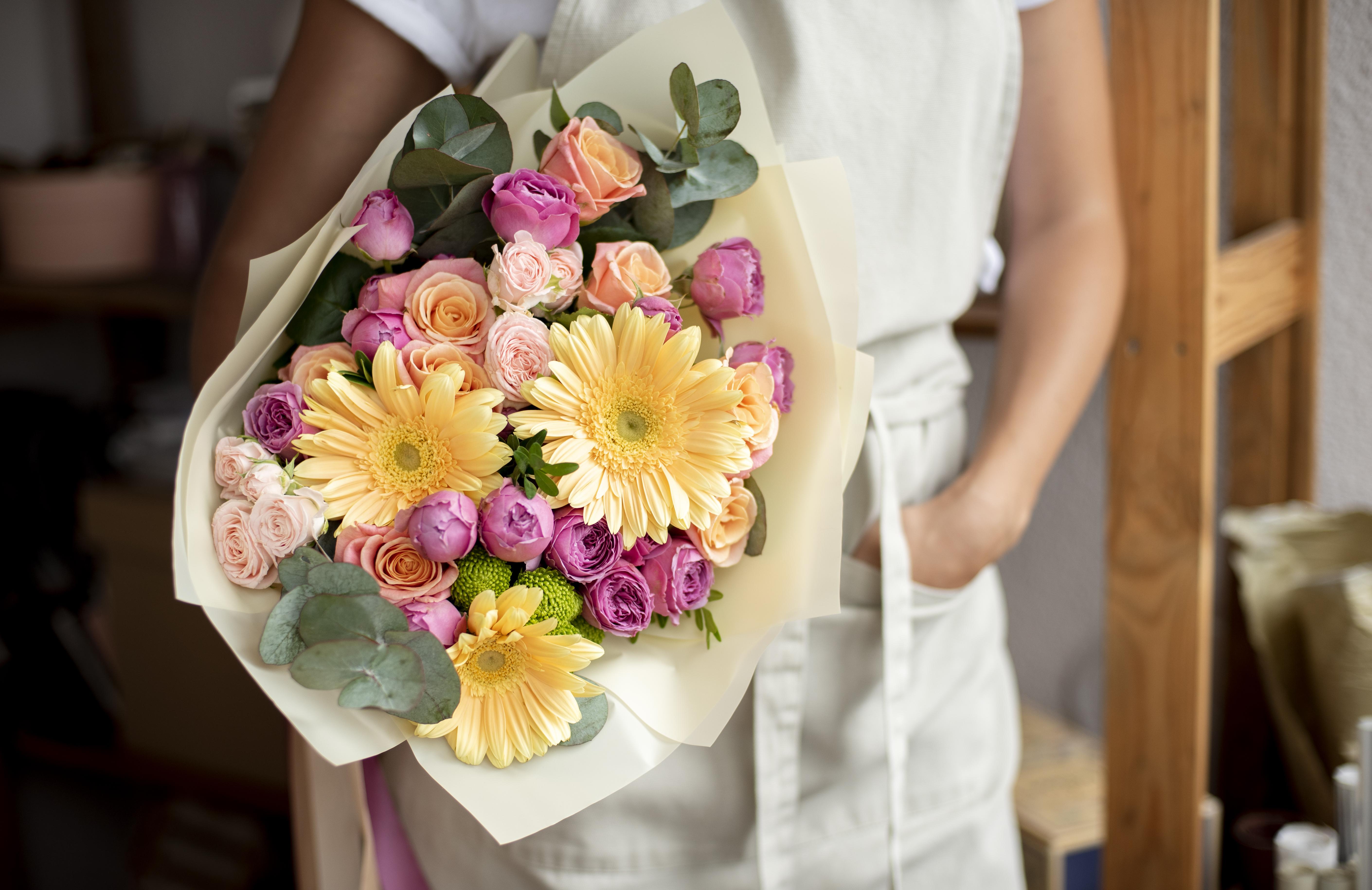 A woman holds a flower bouquet while standing.